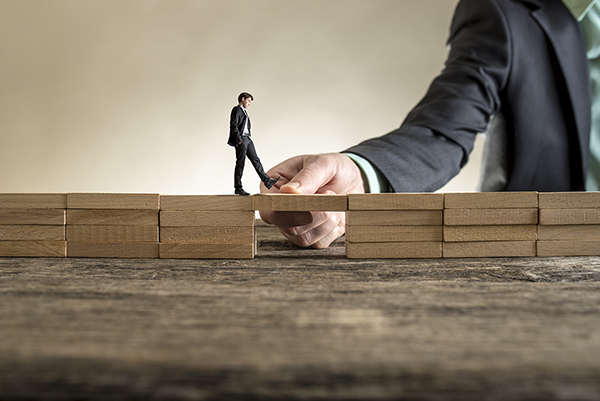 Man solving problems by building bridge with wooden block to span a gap for little businessman walking across.